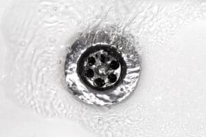 water flowing down sink or tub drain. Sink/tub is white with metal drain.
