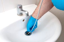 man with blue glove snaking white bathroom sink drain