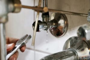 Plumber fixing leaking sink pipes in bathroom