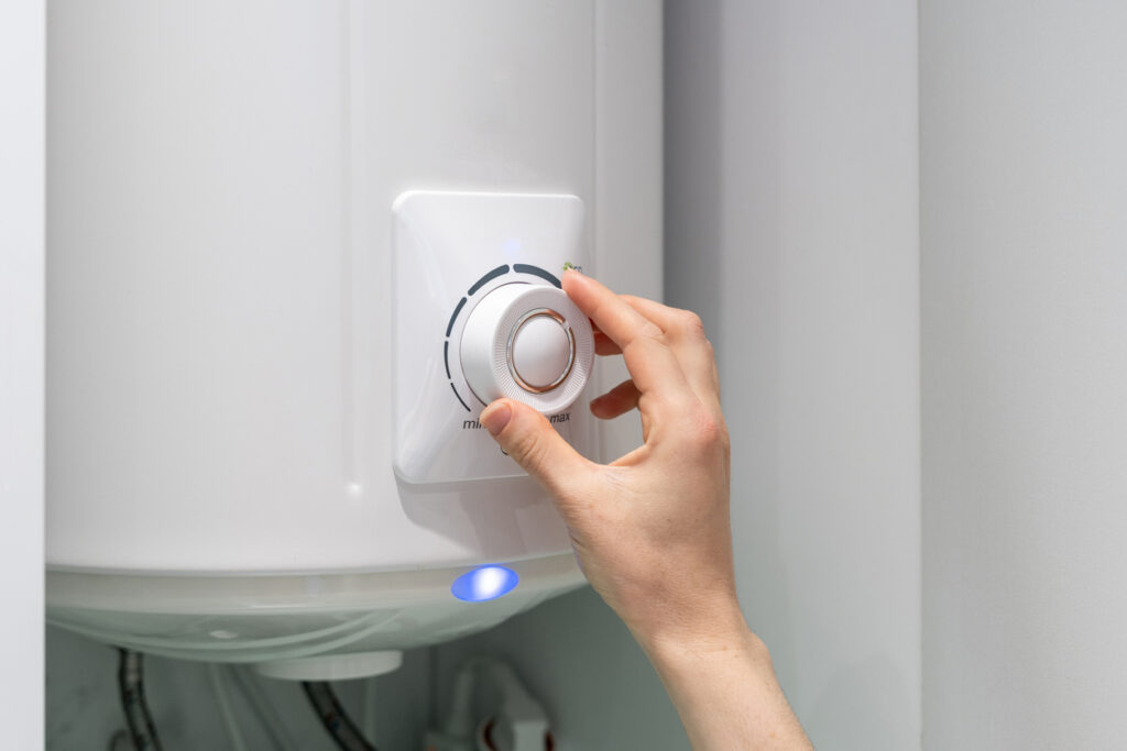 Cropped photo of female adjusting temperature on bathroom electric boiler hanging on wall, using control knob