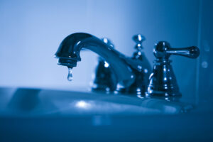 metal faucet dripping into residential bathroom sink. Photo is blue toned. 